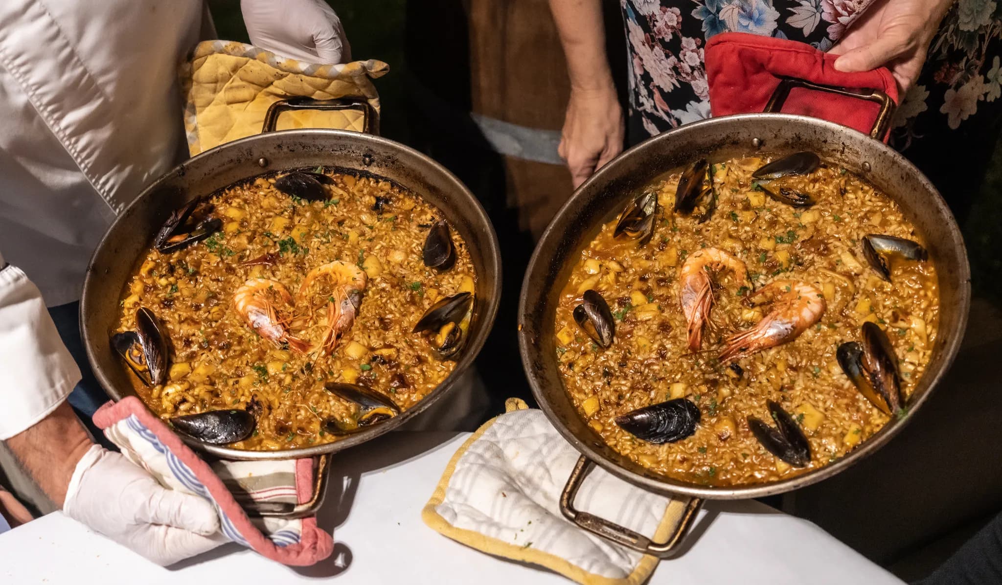 Dos cocineros sostienen dos paellas de marisco recién hechas en sus paelleras