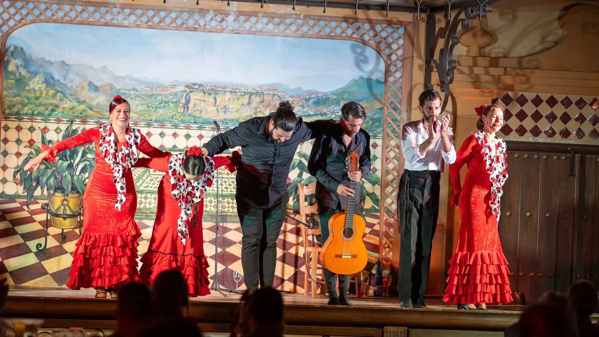 Bailaoras con trajes rojos de volantes y músicos saludando al público al final de un espectáculo flamenco
