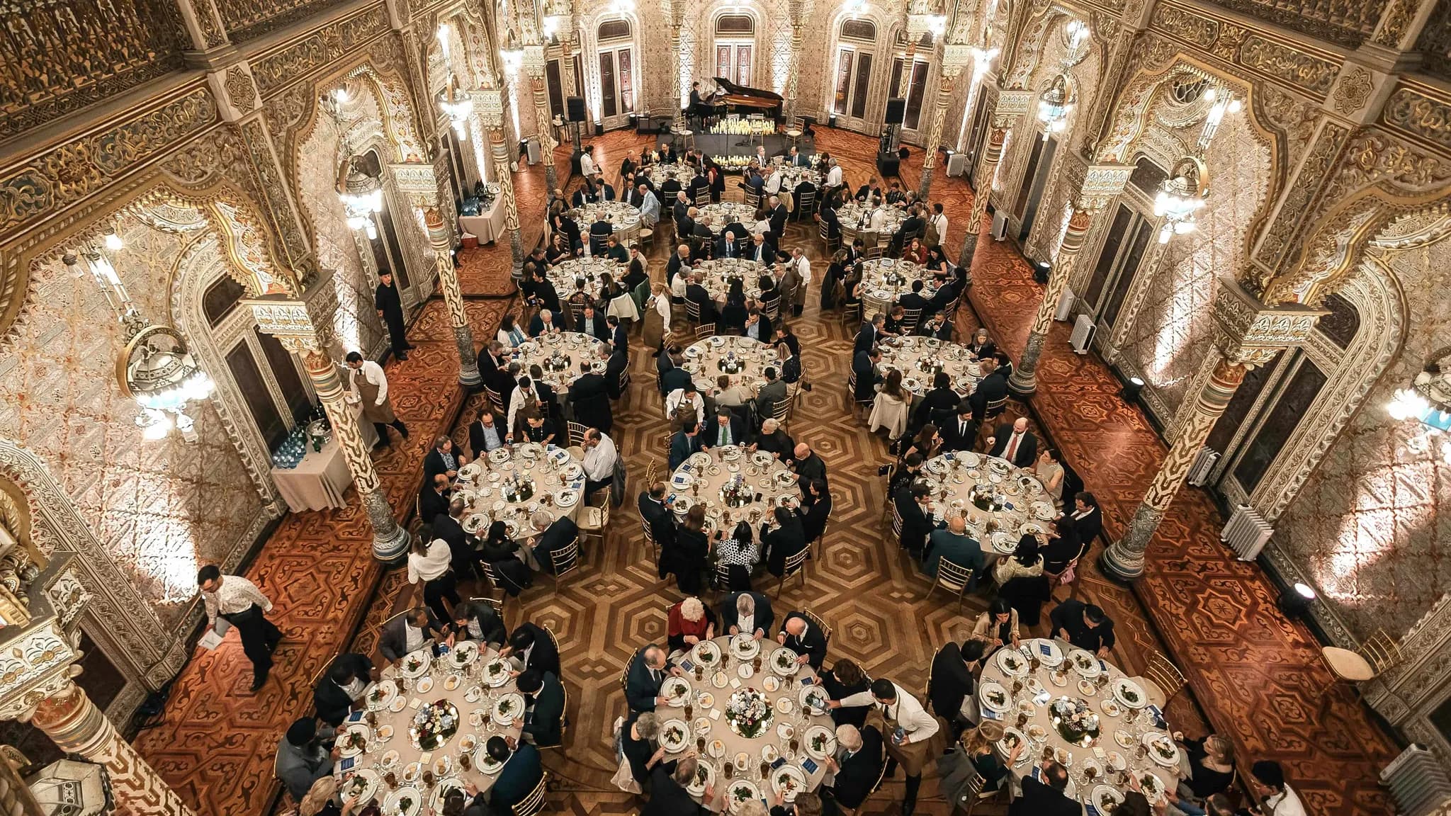 Cena de gala en un salón ornamentado de estilo árabe, con invitados en mesas redondas bajo lámparas de araña
