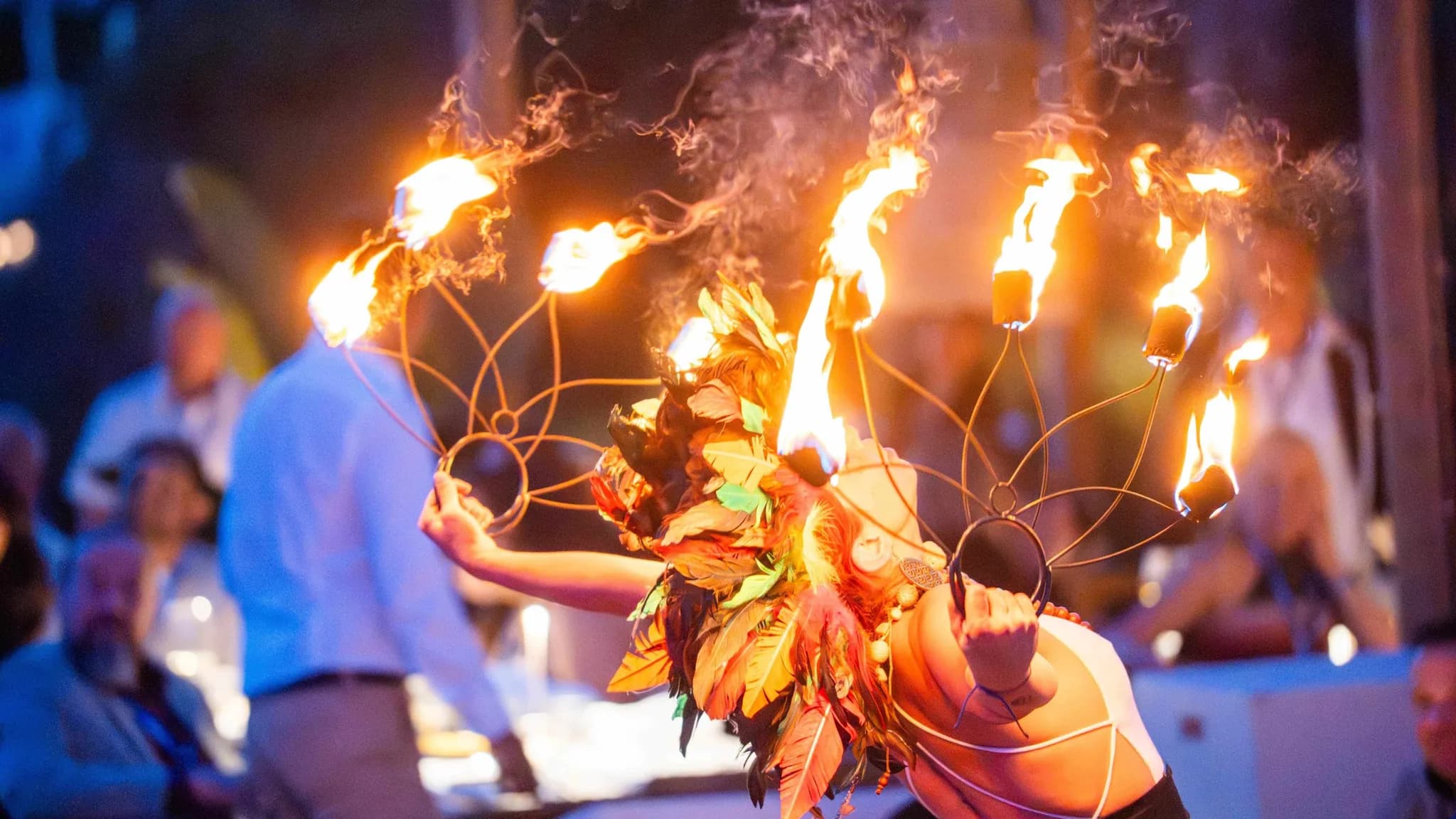 Un artista de fuego con traje de hojas y tocado en llamas amenizando a los invitados en un evento de noche